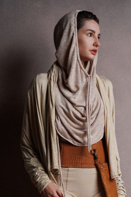 A woman wearing a long beige coat, a brown belt with a large leather pocket, detachable. Burning Man wear, hooded top
